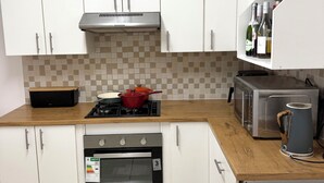 Una cucina con mobili bianchi, un fornello a gas, una pentola rossa, un forno a microonde, un tostapane e un bollitore.