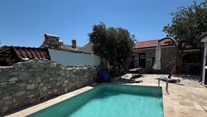 A clear swimming pool with stone walls and a tiled deck, surrounded by buildings with stone facades. - Bahab Plus Guest House (Söke)