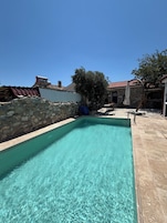 Piscina cristalina con paredes de piedra y un borde de baldosas, rodeada de edificios con fachadas de piedra.