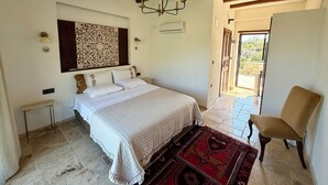 A bedroom with a large bed, a chandelier, a decorative wall piece, a chair, and a view through an open door. - Bahab Plus Guest House (Söke)