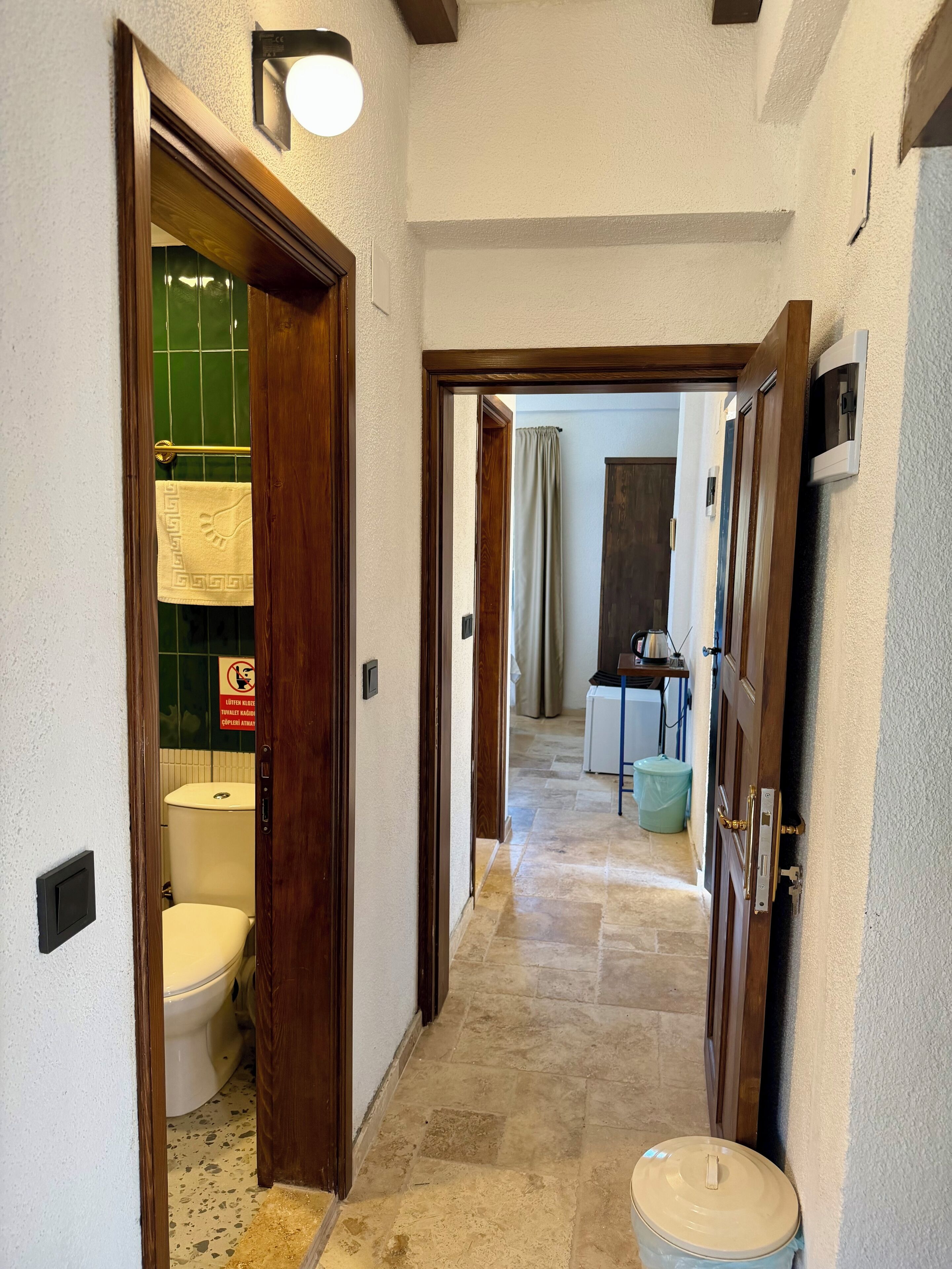Un pasillo con un inodoro, un bote de basura y una puerta que da a otra habitación.