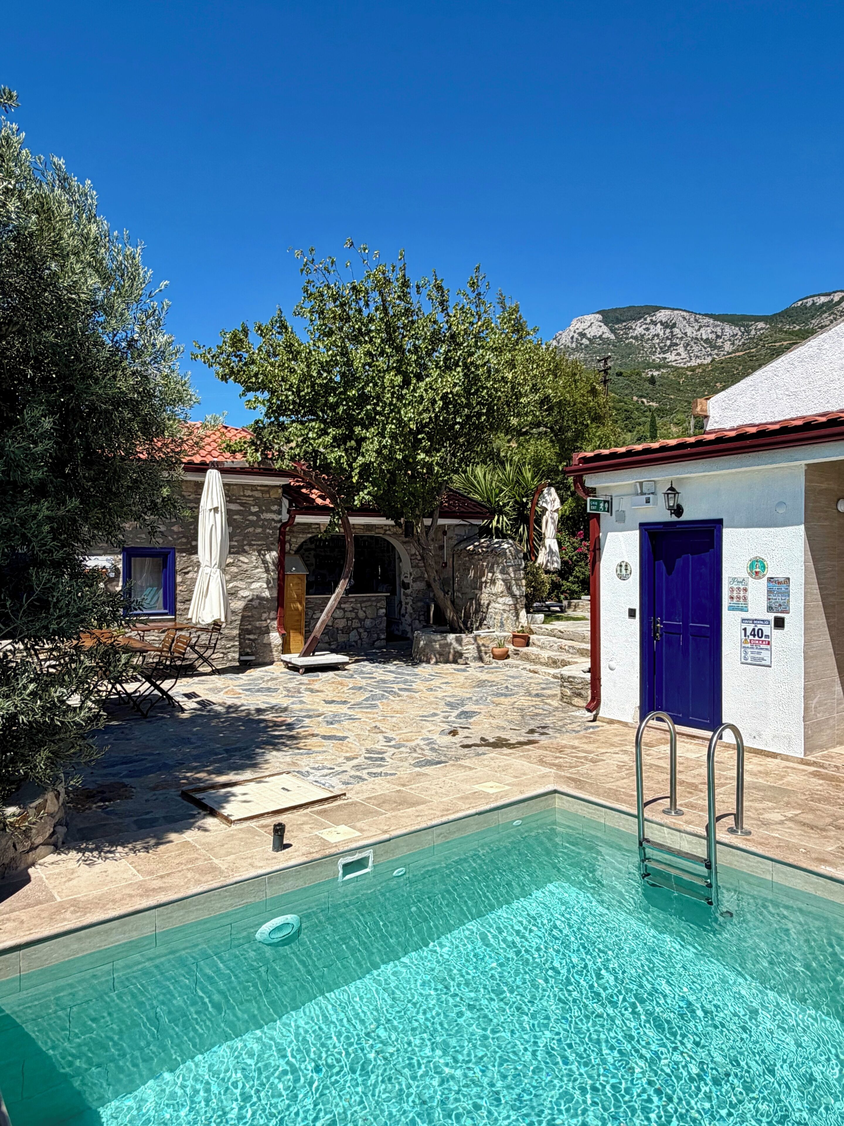 A pool area with a stone floor, a blue door, and a stone building with a red roof.