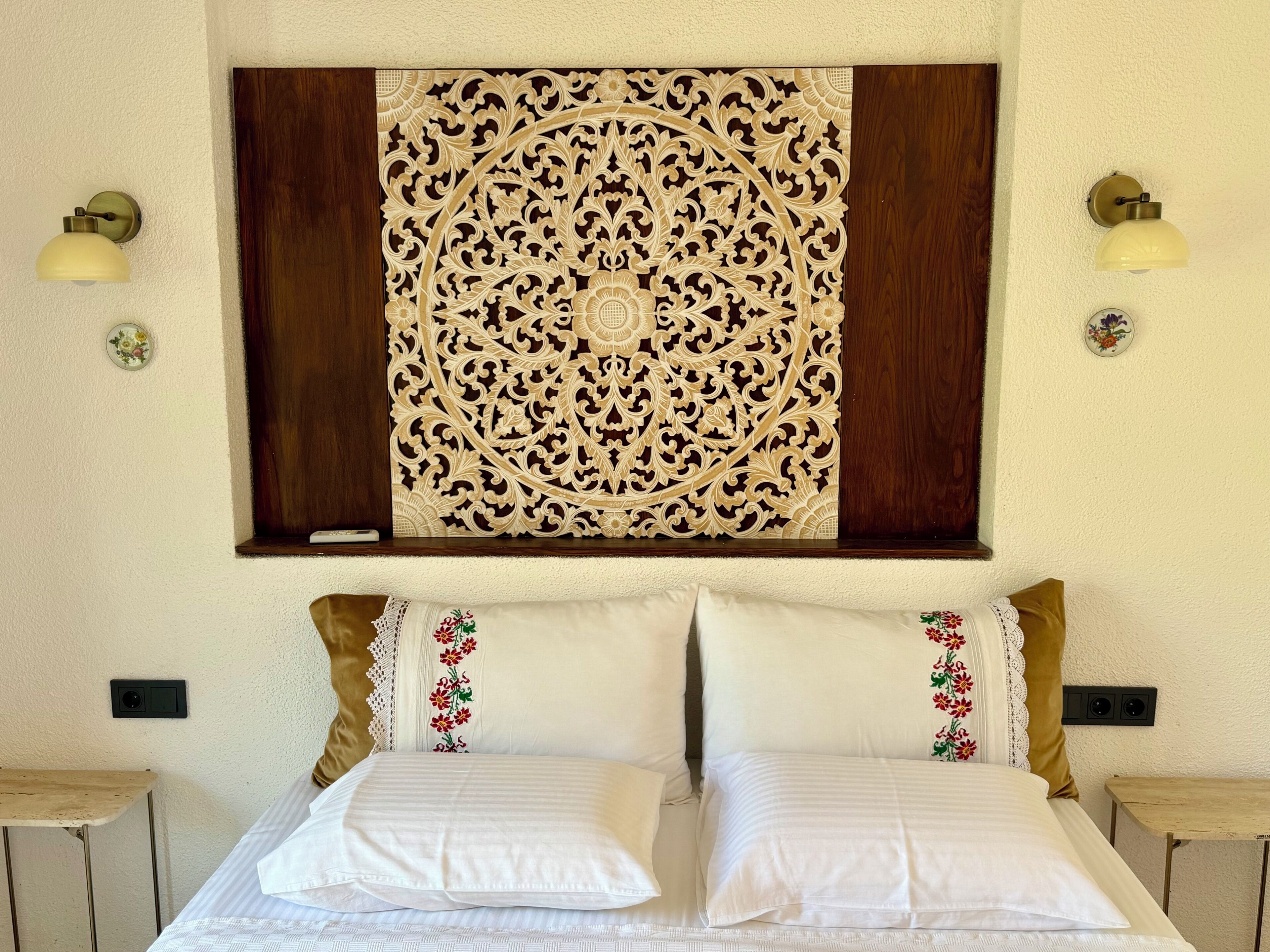A hotel room with a bed, two nightstands, a wall-mounted decorative panel, and two wall-mounted lamps.