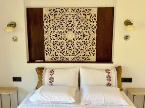 A hotel room with a bed, two nightstands, a wall-mounted decorative panel, and two wall-mounted lamps.