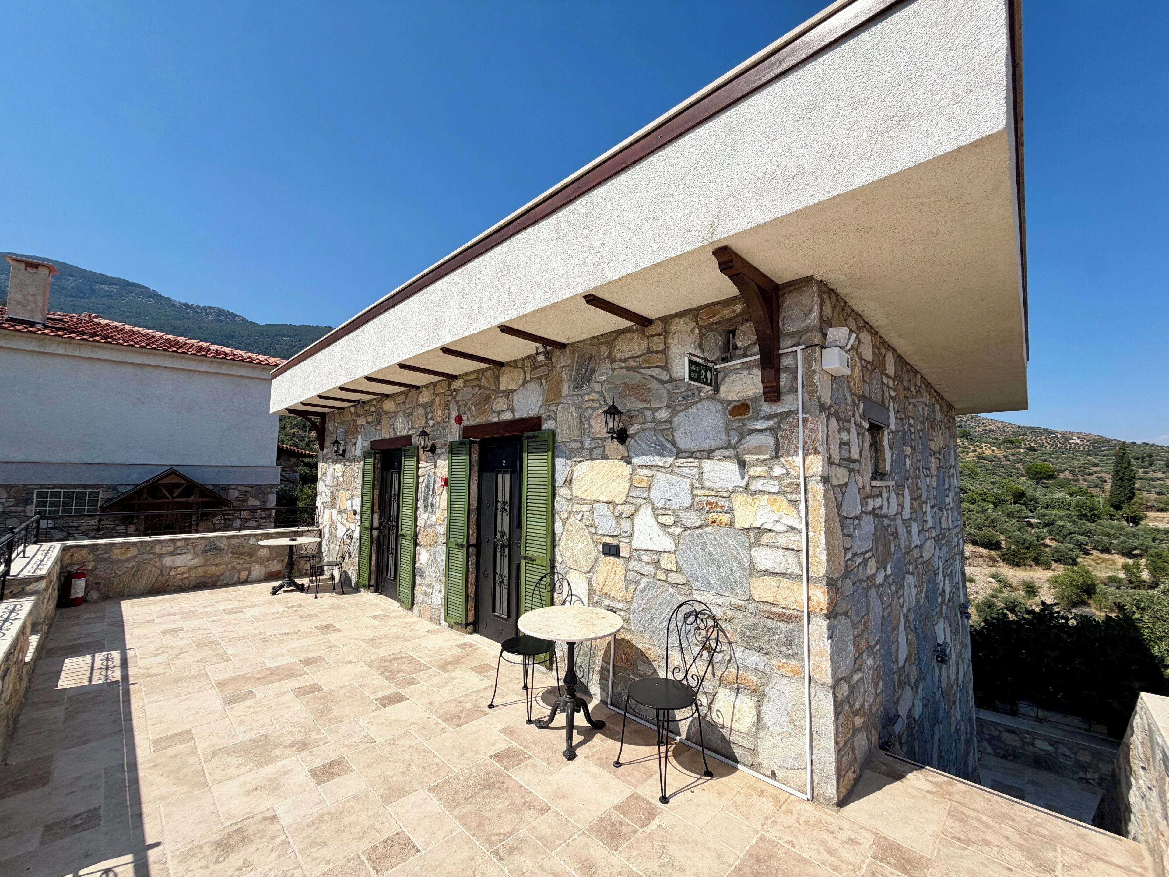 Un edificio de piedra con patio de baldosas, mobiliario exterior y vistas al campo.