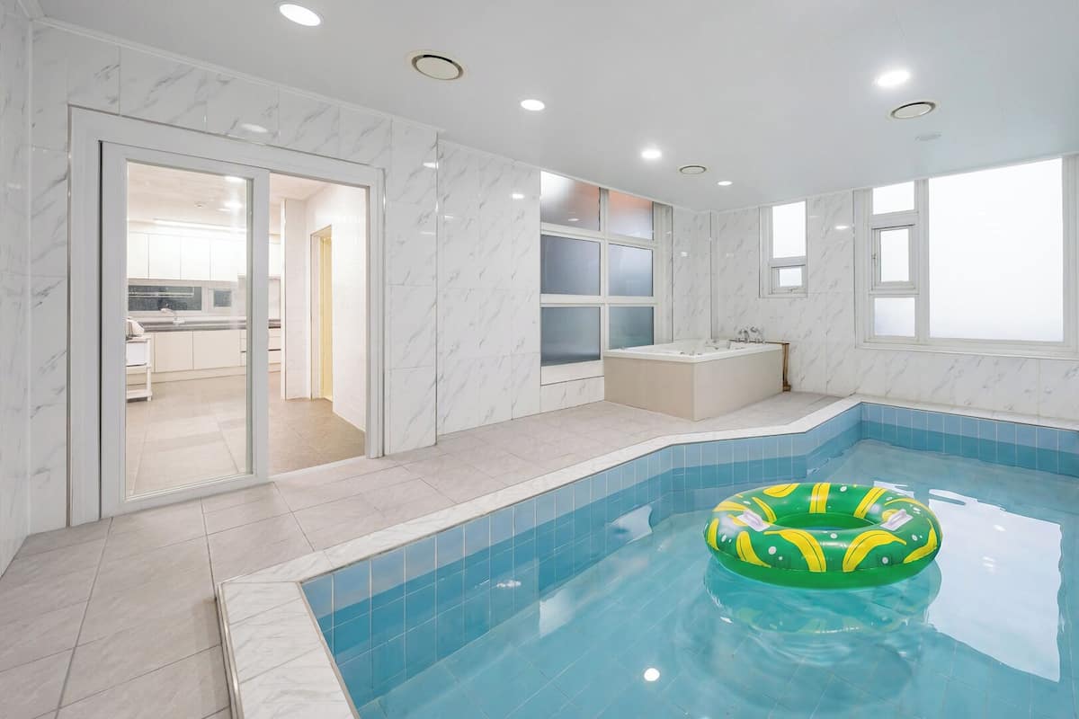 Una piscina interior moderna con un muro de vidrio transparente, una bañera y un ventanal.