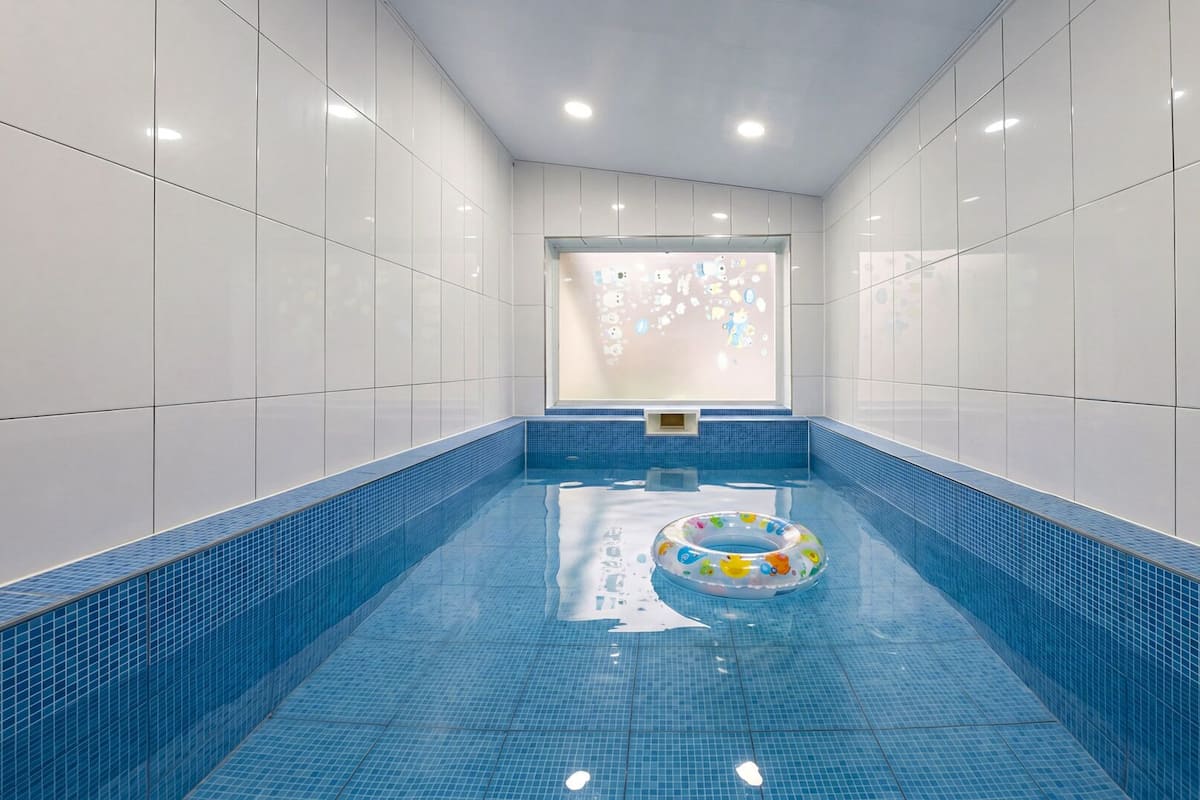 Una piscina con suelo y paredes de azulejos azules, un flotador y una ventana con vista al cielo.