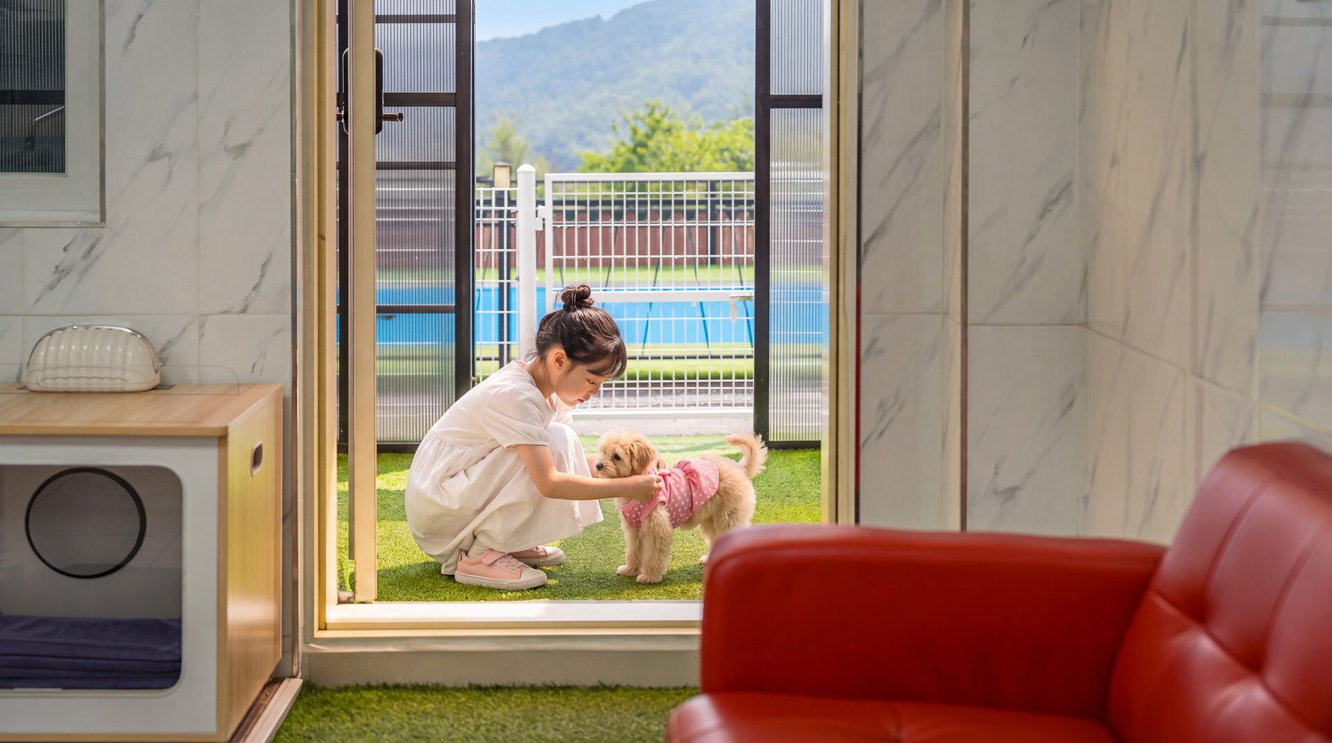 A room with a large sliding glass door leading to a fenced outdoor area, a red couch, and a small table with a toaster.