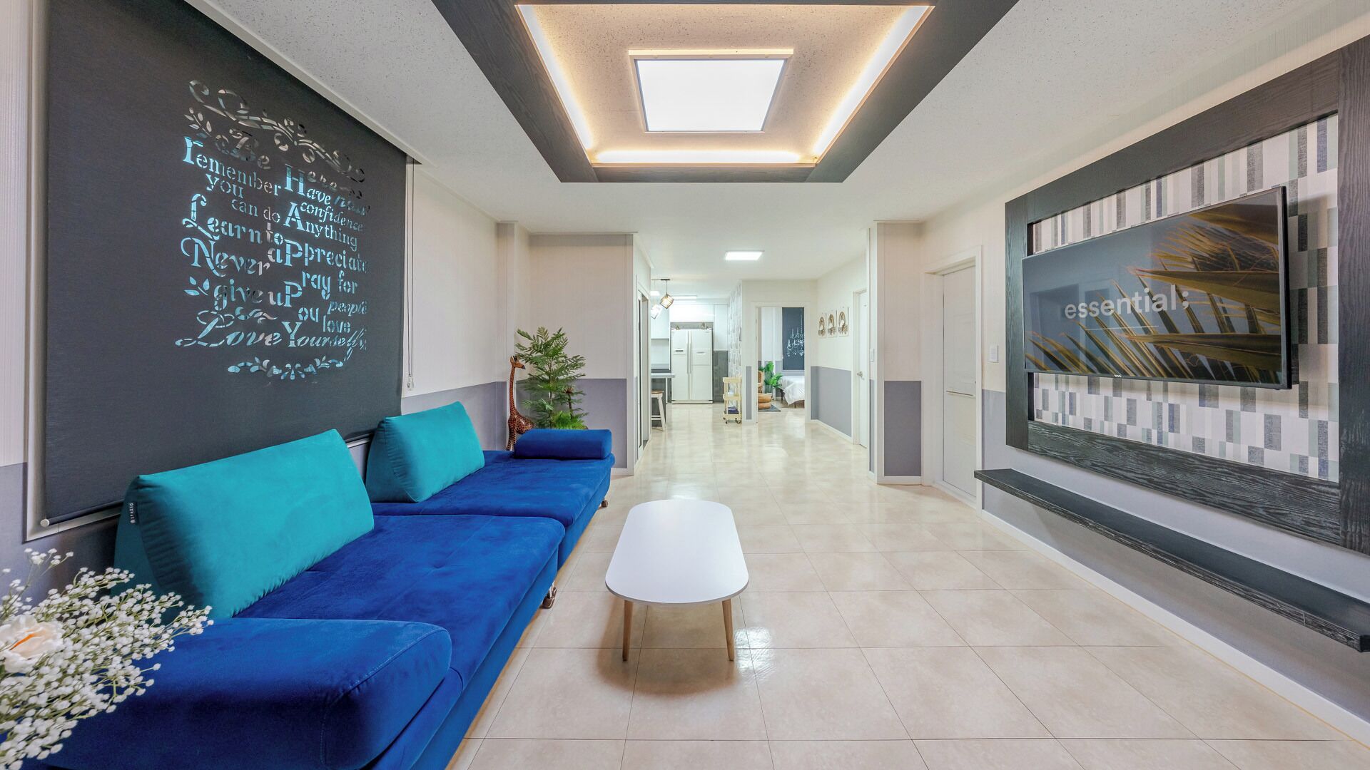 A modern interior with a blue sofa, a white coffee table, a blackboard with inspirational quotes, and a large TV on the wall.