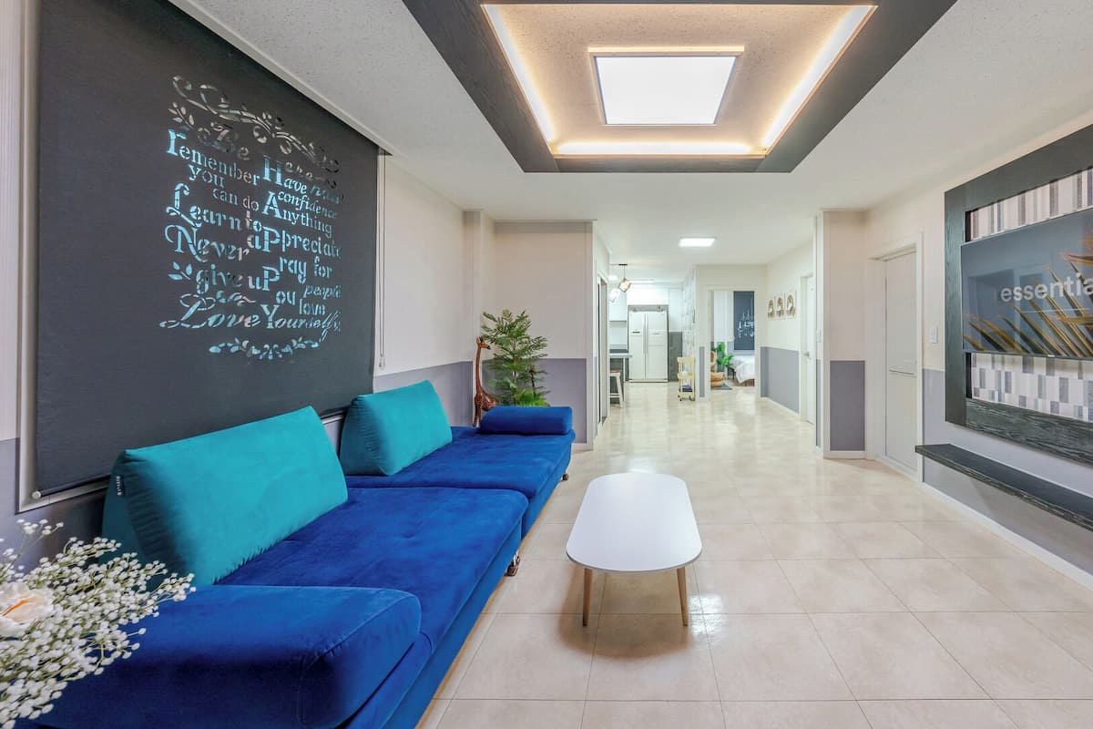 Un interior moderno con un sofá azul, una mesa de centro blanca, una pizarra con citas inspiradoras y un televisor grande en la pared.