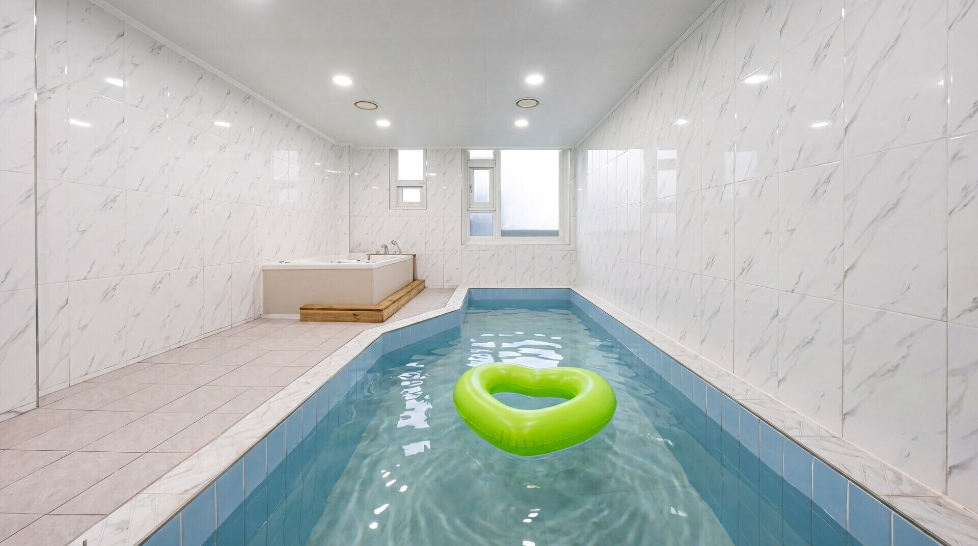 A small indoor pool with a green heart-shaped float, a bathtub, and a window.