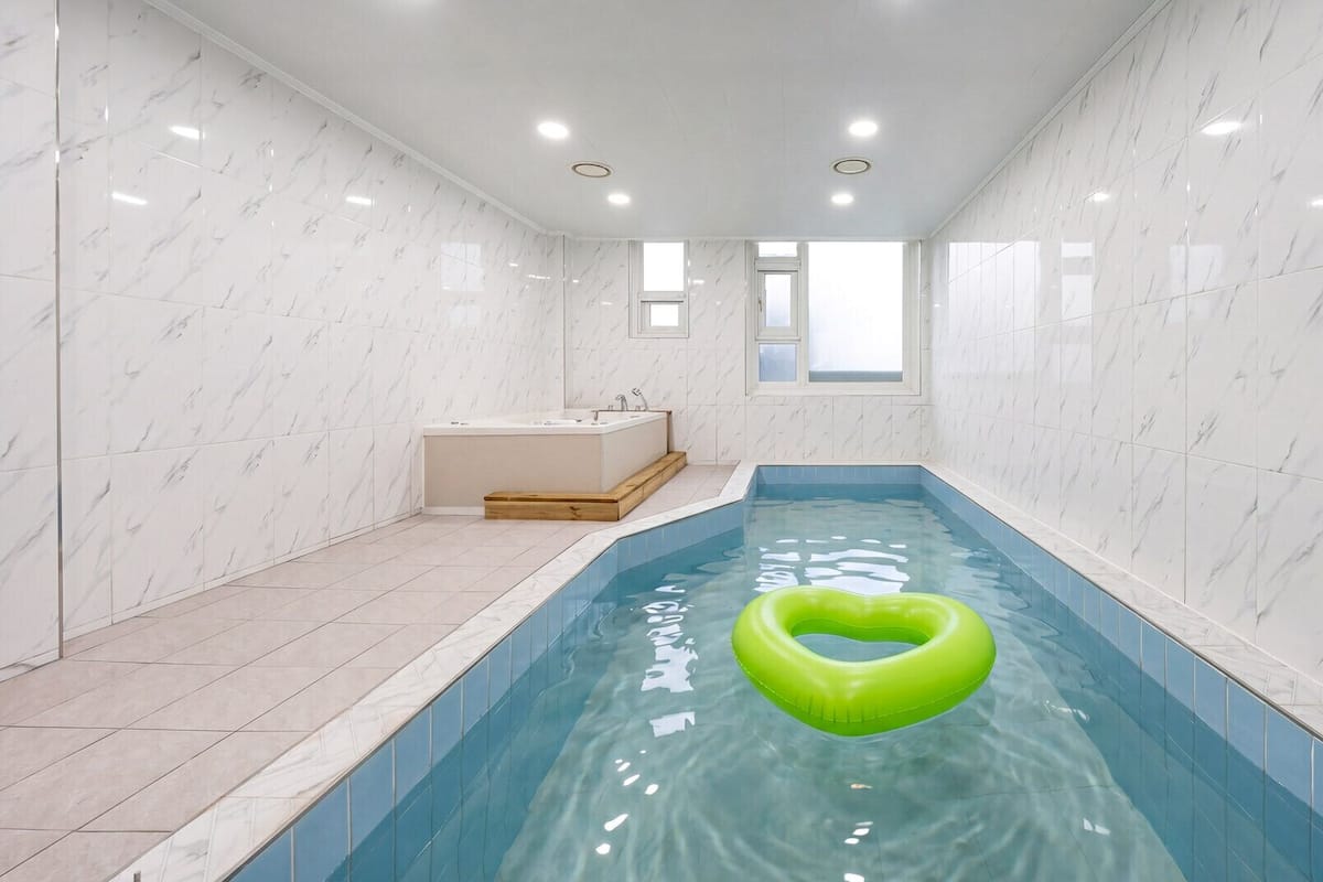 Una piscina interior pequeña con un flotador verde con forma de corazón, una bañera y un ventanal.