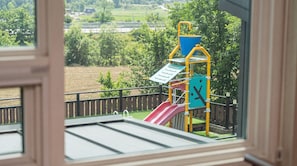 Blick auf einen Spielplatz mit Rutsche und Klettergerüsten durch ein Fenster.