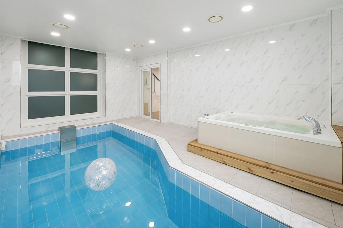Un baño moderno con piscina rectangular, bañera independiente y un amplio ventanal.