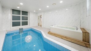 A modern bathroom with a rectangular pool, a freestanding bathtub, and a large window.