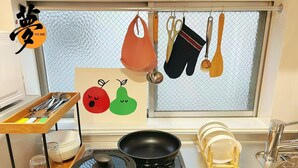 Eine Küche mit Gasherd, einer Bratpfanne, einem Topf, einem Holztablett mit Geschirr und einem Fenster mit hängenden Küchenutensilien.