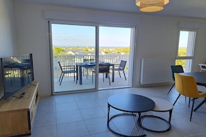 Una habitación con televisión, una mesa de comedor, sillas, sofá y un balcón con vistas.