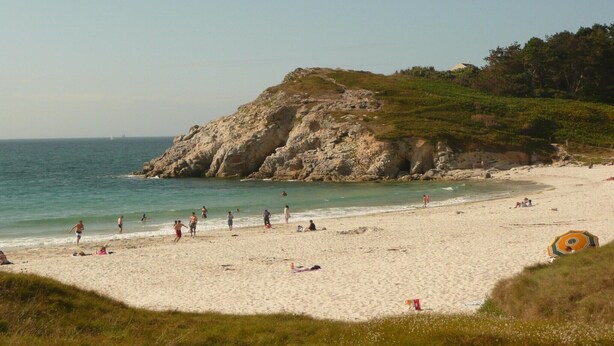 Una playa con gente, un acantilado rocoso y el mar.