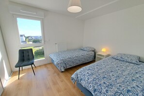 A bedroom with two beds, a chair, a window, and a radiator.