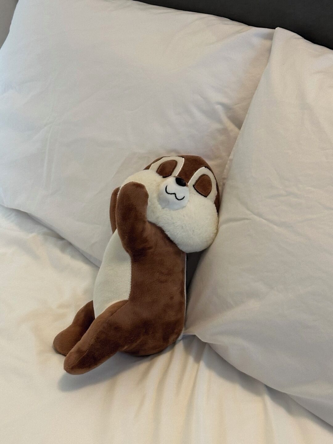 A plush toy on a bed with white bedding.