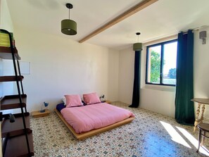 Ein Schlafzimmer mit einem Bett, einem Fenster mit Vorhängen, einer Leiter und einem gemusterten Boden.