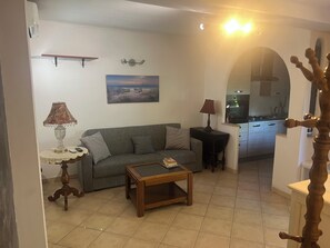 A living room with a sofa, a coffee table, a lamp, a painting, and a kitchen in the background. - Dependance near Rome - 10 min from the sea - Garden and easy parking (Lazio)