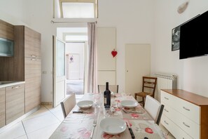 Un coin repas avec une table dressée pour quatre personnes, une bouteille de vin et un téléviseur fixé au mur.