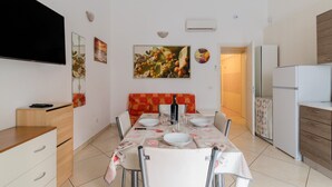 A dining area with a table set for four, a sofa, a TV, and a refrigerator. - 'Corso Roma Home Gallipoli' Apartment with Air Conditioning (Gallipoli)