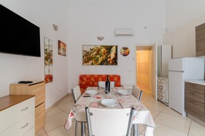 A dining area with a table set for four, a sofa, a TV, and a refrigerator. - 'Corso Roma Home Gallipoli' Apartment with Air Conditioning (Gallipoli)