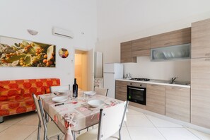 A modern kitchen with a built-in oven, a dining area with a table set for two, and a colorful sofa. - 'Corso Roma Home Gallipoli' Apartment with Air Conditioning (Gallipoli)