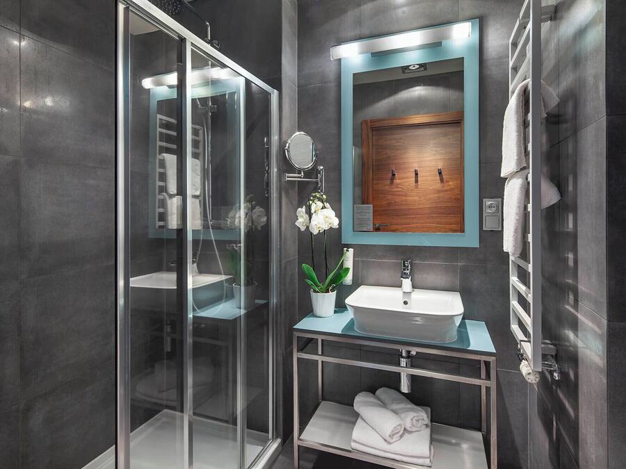 A modern bathroom with a glass shower enclosure, a white sink with a wooden vanity, and a mirror with a wooden frame.