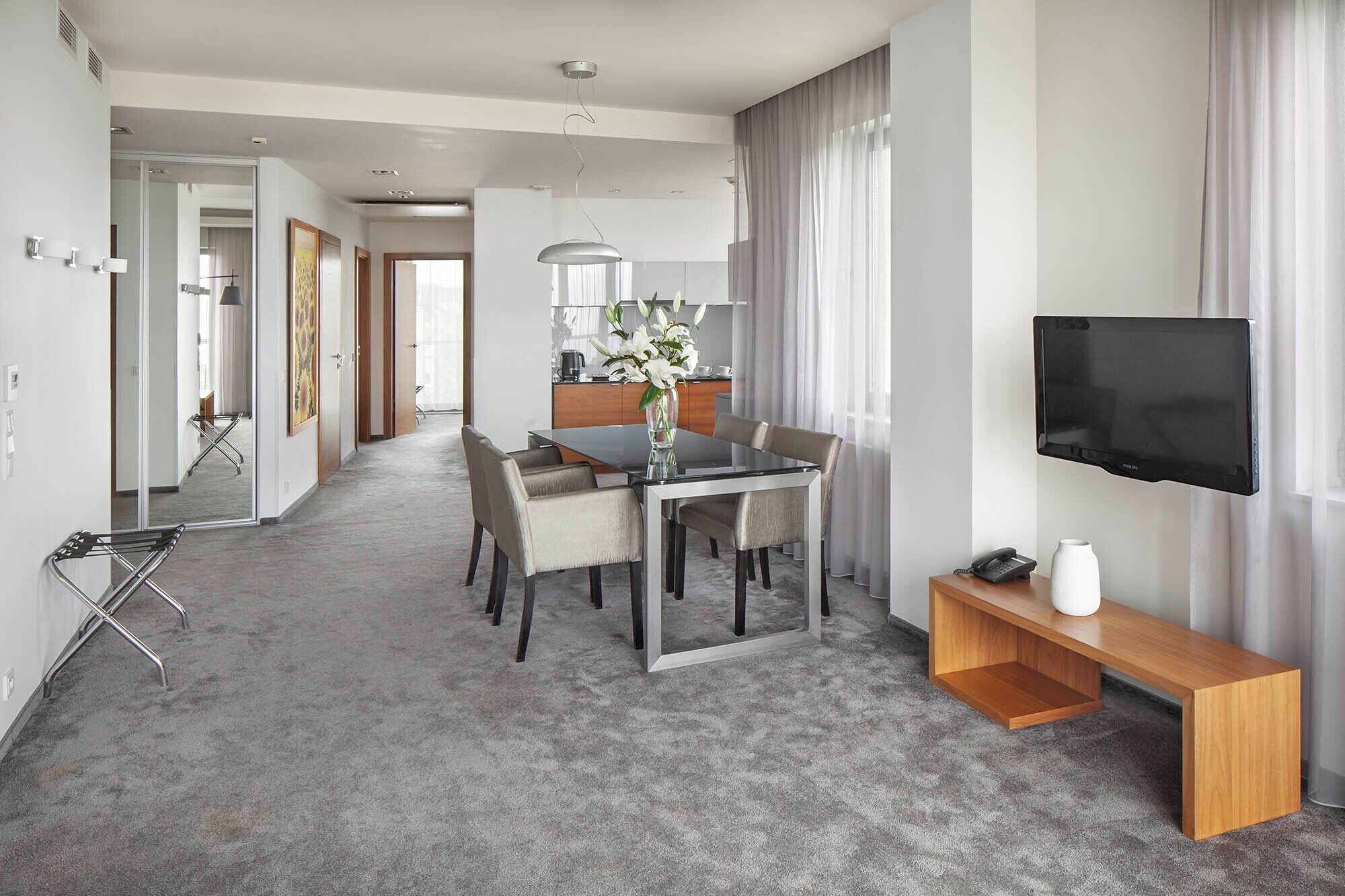 Moderni hotellihuone, jossa on ruokailutila, televisio ja kylpyhuone, joka on näkyvissä lasiovesta.