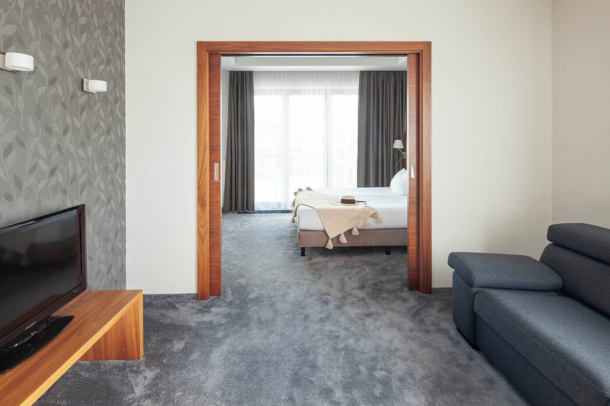 Hotelkamer met televisie, een bank, een bed met hoed en deken, en uitzicht door een deur.