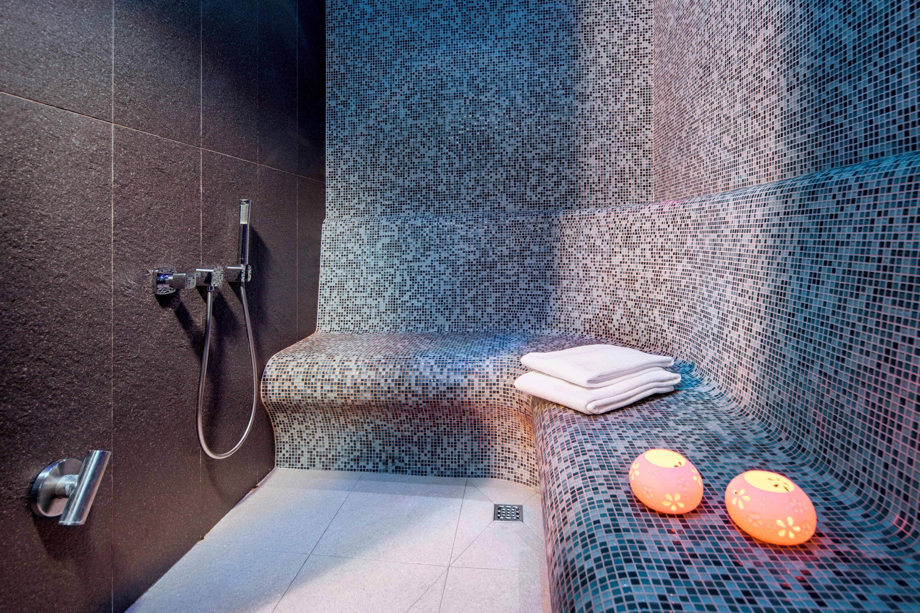 A modern bathroom with a shower, a towel rack, and a bench with decorative lights.