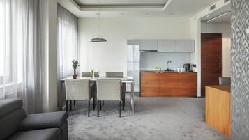A modern hotel room with a dining area, kitchenette, and a grey sofa.