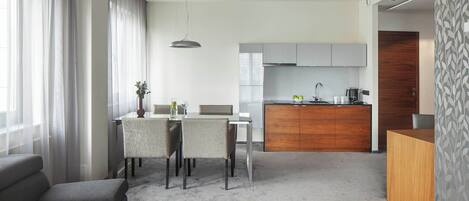 A modern hotel room with a dining area, kitchenette, and a grey sofa.