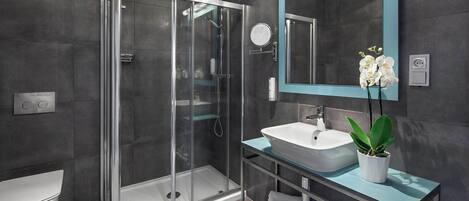 Un baño moderno con ducha de vidrio, un lavamanos blanco, un espejo con marco azul aguamarina y una orquídea en maceta.