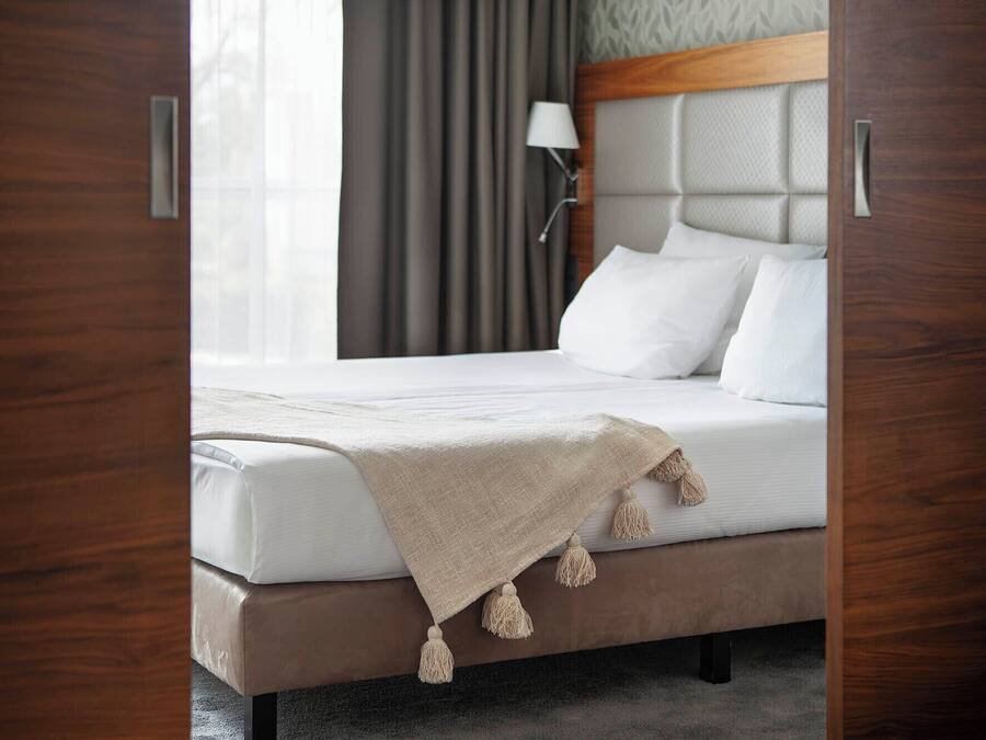 A hotel room with a bed, a headboard, a lamp, and a window with curtains.