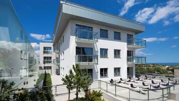 A modern building with multiple balconies, a rooftop terrace with seating, and a clear view of the sea.
