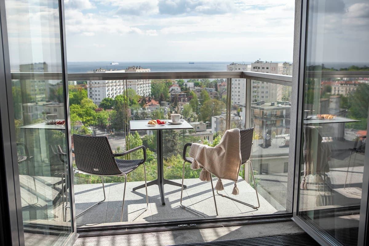 Een balkon met twee stoelen, een tafeltje met een kopje en gebak, en uitzicht op de stad en de zee.