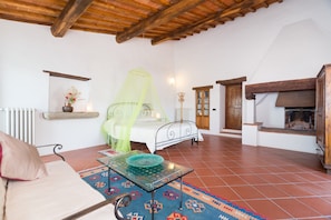 Une pièce comprenant un lit, une table avec un bol, un radiateur, une étagère avec un vase, une fenêtre et une cheminée.