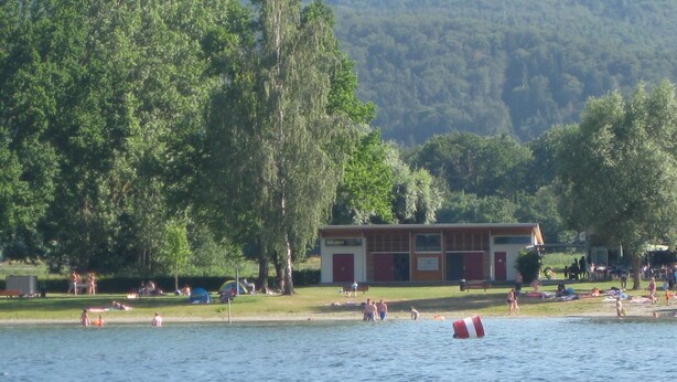 Vista para o lago com um edifício, árvores e pessoas à beira da água.