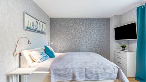 Quarto moderno com cama, mesa de cabeceira, televisão e TV montada na parede.