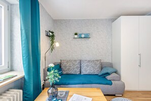 A modern living room with a grey sofa, teal curtains, a wooden coffee table, and a white wardrobe.