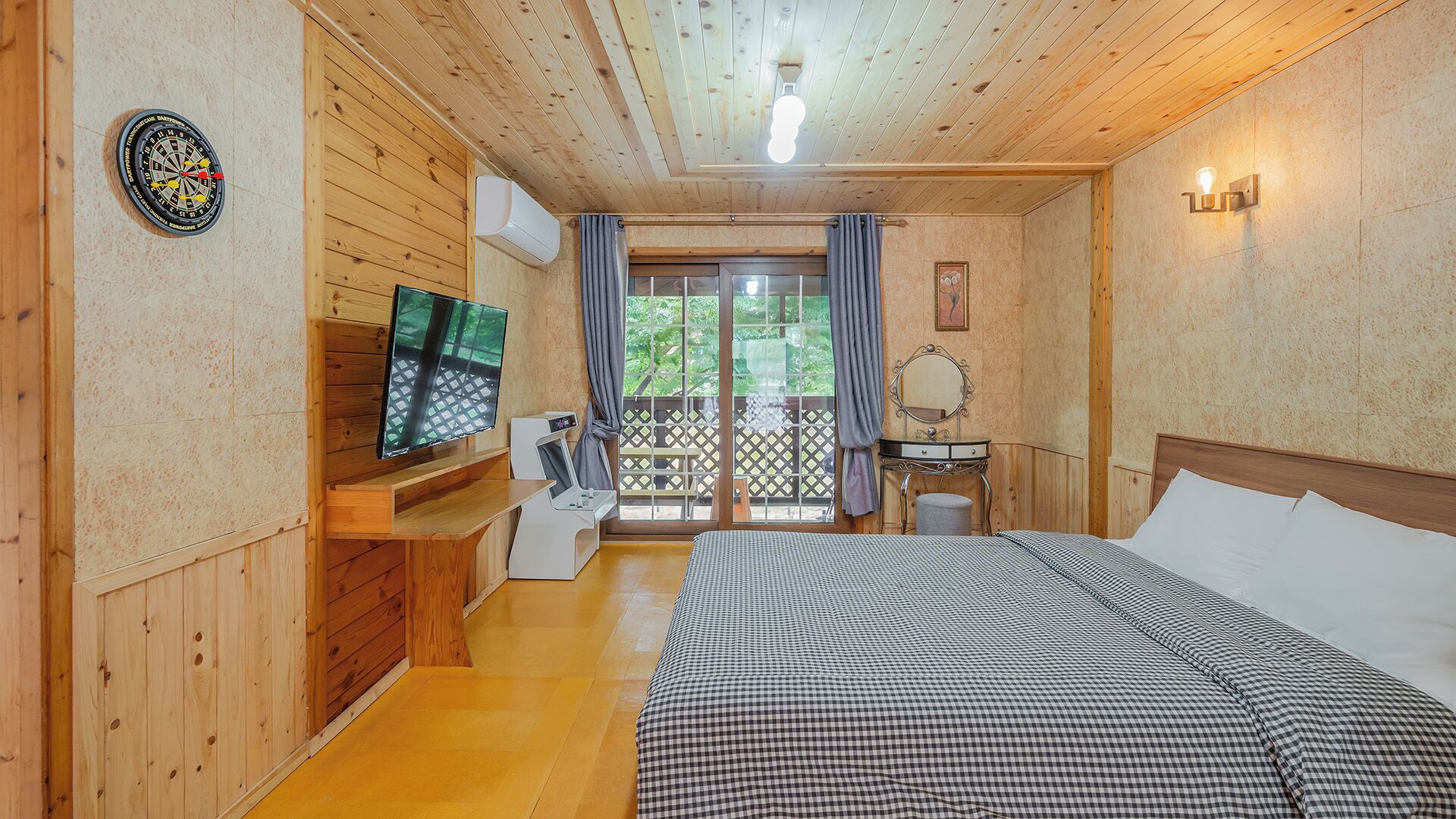 Una habitación con paneles de madera, una cama, un televisor, un escritorio y un ventanal con cortinas.