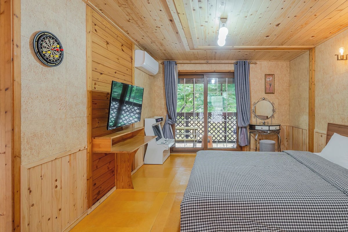 Ein Zimmer mit Holzwandverkleidung, einem Bett, einem Fernseher, einem Schreibtisch und einem Fenster mit Vorhängen.