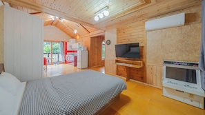 Ein Schlafzimmer mit Bett, Fernseher, einer kleinen Küchenzeile und einer Klimaanlage.