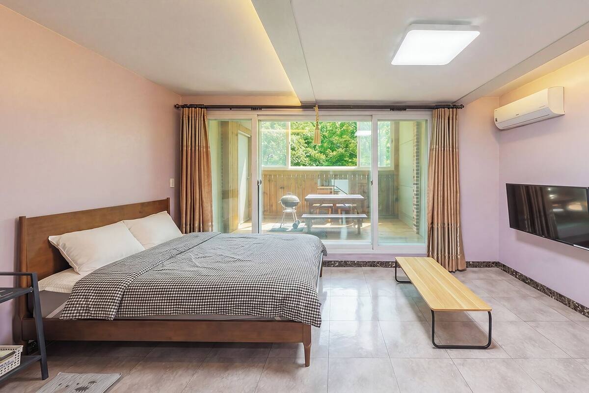 A bedroom with a bed, a bench, a TV, and a sliding glass door leading to an outdoor area with a table and chairs.