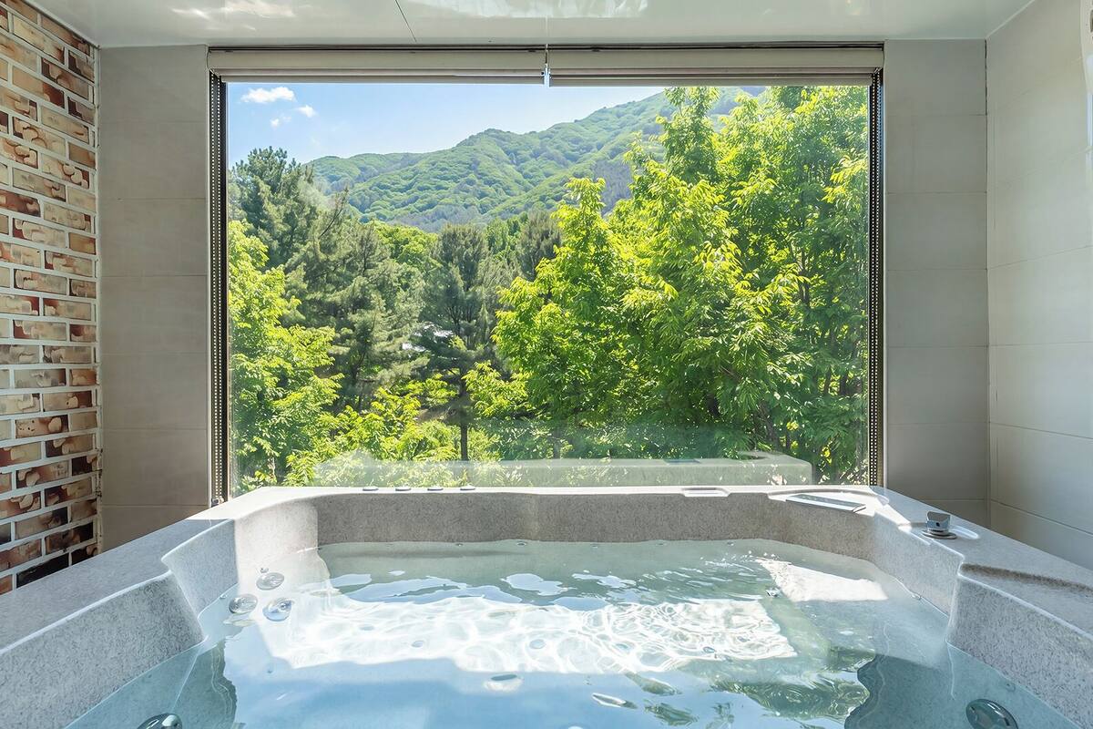 A bathroom with a bathtub, a large window, and a brick wall.