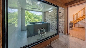 Ein modernes Badezimmer mit Glasabtrennung, einer Whirlwanne und Blick auf eine bewaldete Gegend.